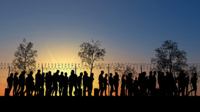 A group of people standing at a border fence