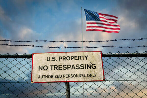 Sign on fence reading, “U.S. property No Trespassing (Authorized Personnel Only)”; American flag in the background