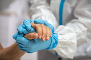 Two gloved hands compassionately embraces a non-gloved hand