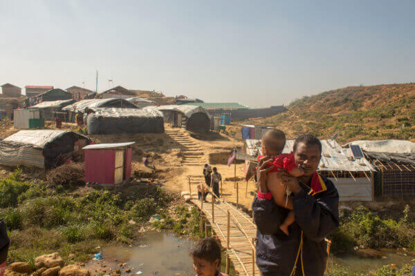 A Rohingya refugee walking with his child in his arms.