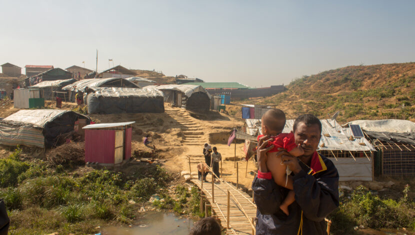 A Rohingya refugee walking with his child in his arms.