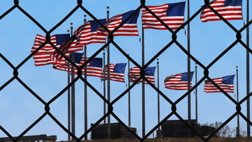 Several American flags seen through a chainlink fence