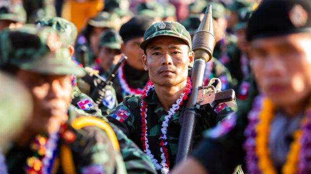 A member of the Burmese military surrounded by his comrades; he is holding a weapon