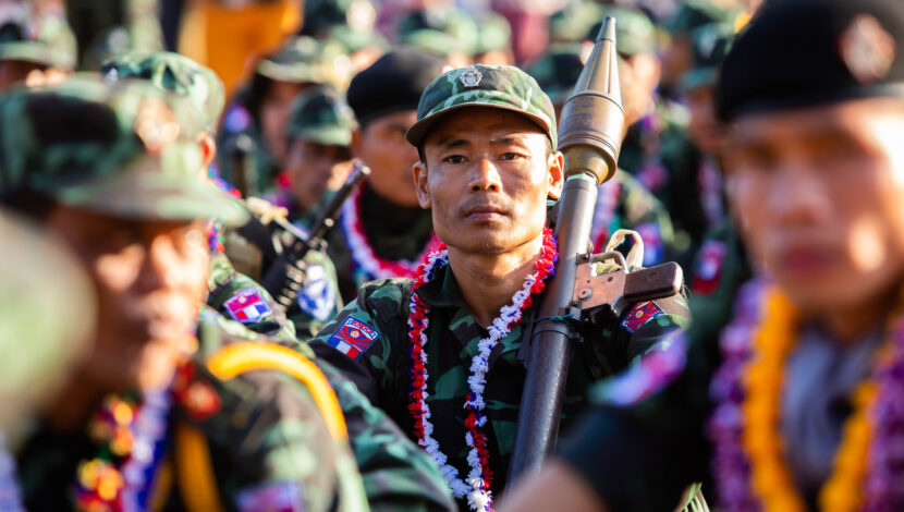 A member of the Burmese military surrounded by his comrades; he is holding a weapon