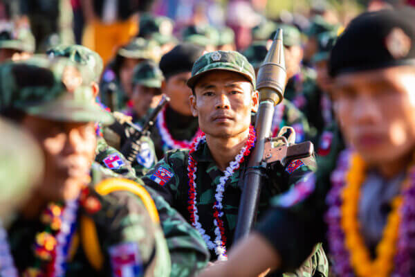 A member of the Burmese military surrounded by his comrades; he is holding a weapon